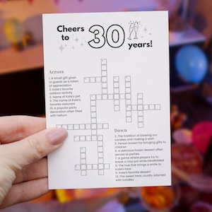 Può includere: Una carta bianca con un cruciverba per una festa di compleanno per i 30 anni. La carta recita "Cheers to 30 years!" con un cruciverba sotto. Il puzzle include indizi come "L'attività all'aperto preferita di Kate."