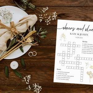 Wedding crossword puzzle displayed on rustic wooden table with linen napkin, gold cutlery, wedding rings, eucalyptus and baby's breath, "cheers and clues" header design