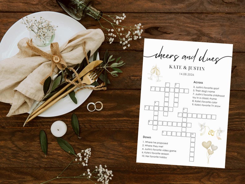 Wedding crossword puzzle displayed on rustic wooden table with linen napkin, gold cutlery, wedding rings, eucalyptus and baby's breath, "cheers and clues" header design