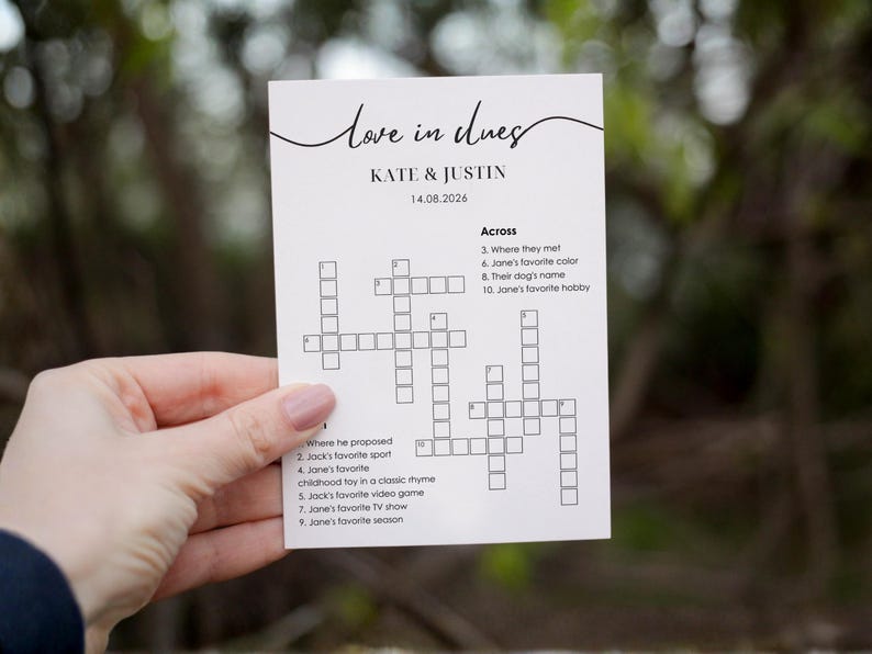 Minimalist wedding crossword puzzle card held in hand, "love in clues" script header, couple names and wedding date, across and down clues based on the couple's love story