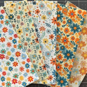 May include: Six fabric swatches with a floral pattern. The fabric is a light beige color with a variety of blue, orange, and yellow flowers. The flowers are all different sizes and shapes.