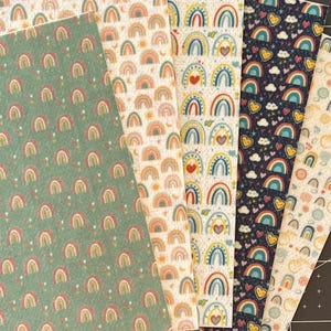 May include: Five different fabric sheets with rainbow patterns. The sheets are all white with different colored rainbows and other designs. The designs include hearts, clouds, and stars. The sheets are all different sizes.