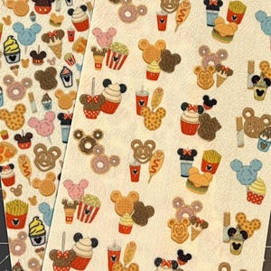 May include: Two sheets of patterned paper featuring various cartoon food and character designs. The designs include Mickey Mouse-shaped waffles, donuts, ice cream, popcorn, and french fries. The color palette includes red, yellow, brown, and blue.