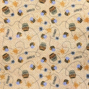 May include: A beige fabric with a repeating pattern of honey jars, bees, and stars. The text "Honey" is repeated throughout the fabric.
