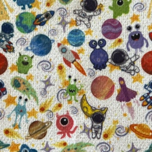 May include: A white fabric with a repeating pattern of colorful space-themed illustrations. The pattern includes astronauts, planets, stars, comets, and aliens.