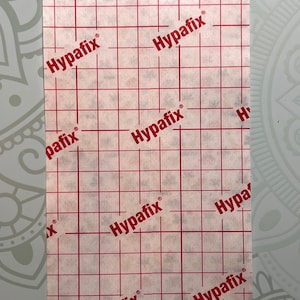 Op de afbeelding: Witte plakband met een rasterpatroon en de tekst "Hypafix" die overal herhaald wordt.