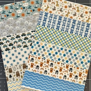 May include: Two sheets of patterned fabric featuring various designs. One sheet has sailboats, suns, and clouds. The other has teddy bears, stars, and cars. Colors include blue, yellow, and white. The fabric appears to be for baby or children's crafts.