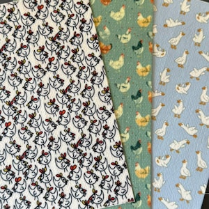 May include: Three sheets of patterned material. One sheet has a repeating pattern of black and white chickens with red and yellow accents. The second sheet has a repeating pattern of chickens in various colors on a green background. The third sheet has a repeating pattern of white geese on a blue background.