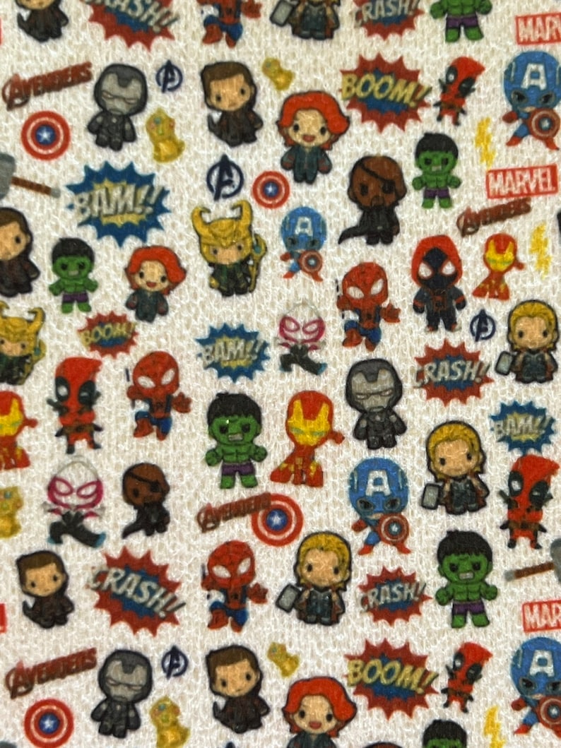 Op de afbeelding: Een witte stof met een herhalend patroon van cartoon superhelden uit het Marvel-universum. De personages omvatten Iron Man, Captain America, Thor, Hulk, Spider-Man, Black Widow en Deadpool. De stof bevat ook de woorden "BOOM!" "BAM!" en "CRASH!" in een comic-boek lettertype.