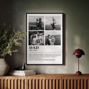 May include: A framed black and white print featuring four family photos. The word "DAD" is prominently displayed with a definition below. The print includes a quote about fathers. The frame is black and sits on a wooden cabinet.