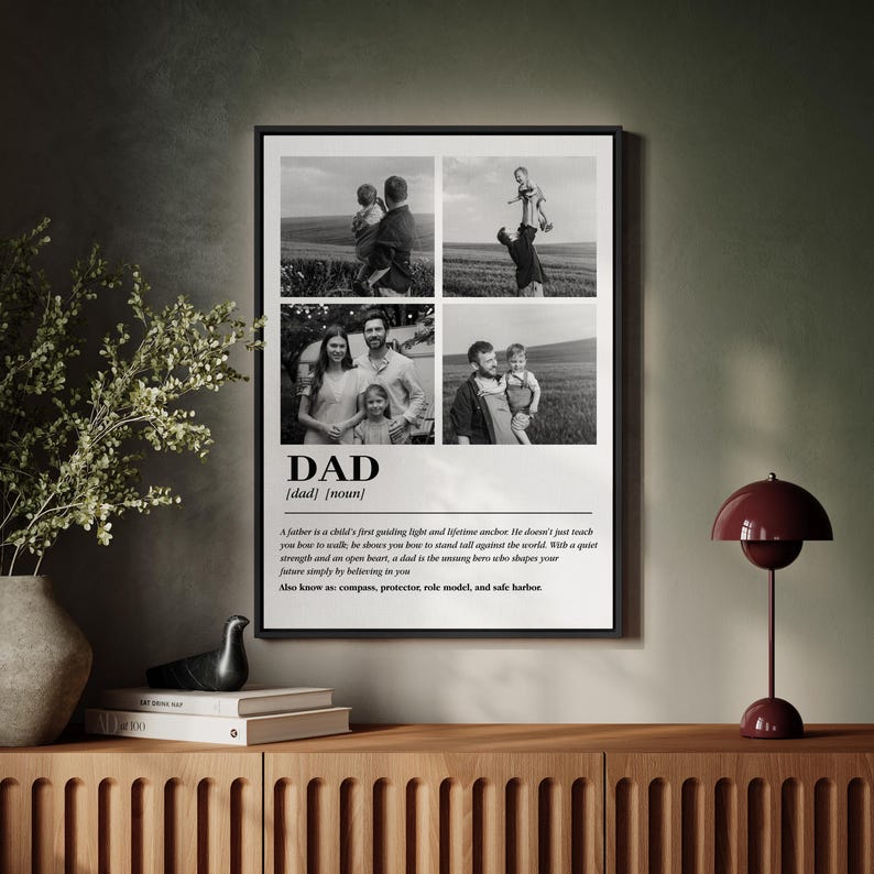 May include: A framed black and white print featuring four family photos. The word "DAD" is prominently displayed with a definition below. The print includes a quote about fathers. The frame is black and sits on a wooden cabinet.