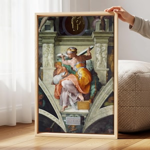 May include: Framed art print featuring a Renaissance-style fresco. The artwork depicts figures in vibrant colors, including orange, yellow, and pink, set against a backdrop of architectural details. The frame is made of light-colored wood.