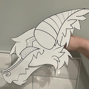 May include: A white, stylized illustration of a horned creature's head. The design features intricate line work, including spirals, circles, and striped details on the horns. The head is held against a neutral background.