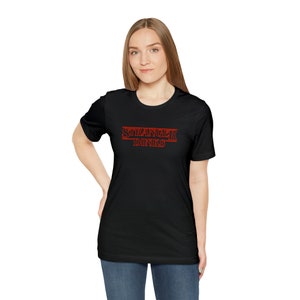 Könnte beinhalten: Schwarzes T-Shirt mit einer roten Grafik, auf der "Stranger Dinks" in einer Schriftart steht, die dem Stranger Things-Logo ähnelt.