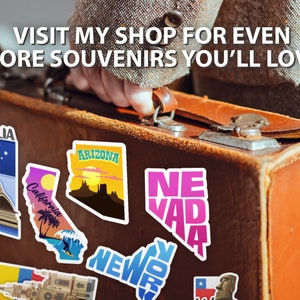 Puede incluir: Una maleta vintage marr&oacute;n con pegatinas de colores de estados y pa&iacute;ses. Las pegatinas incluyen Australia, California, Arizona, Nevada, Nueva York y Chile. El texto en la maleta dice "VISIT MY SHOP FOR EVEN MORE SOUVENIRS YOU'LL LOVE."