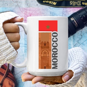 May include: White ceramic mug with a graphic of a red Moroccan flag, a brown building with a star, and the word "MOROCCO" in black text.