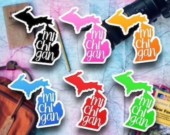 May include: Six Michigan state outline stickers in different colors: black, pink, orange, blue, red, and green. Each sticker has the text "mi chi gan" in white.