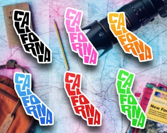 May include: Six colorful stickers shaped like the state of California, each with the word "CALIFORNIA" spelled out in a unique way. The stickers are black, pink, orange, red, blue, and green.