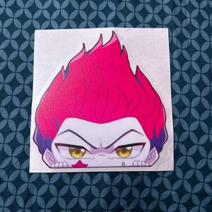 Puede incluir: Una pegatina con un personaje de dibujos animados con cabello rojo, ojos amarillos y una estrella rosa en la mejilla. El personaje est&aacute; mirando al espectador mientras se asoma por encima de una superficie.