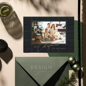 May include: A rectangular Christmas greeting card featuring a dark green plaid border and a central photograph of a family with a dog near a Christmas tree. The card displays the text Merry Christmas and The Hill Family in a gold script font.