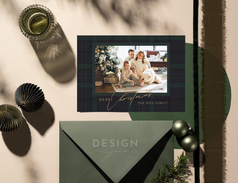 May include: A rectangular Christmas greeting card featuring a dark green plaid border and a central photograph of a family with a dog near a Christmas tree. The card displays the text Merry Christmas and The Hill Family in a gold script font.