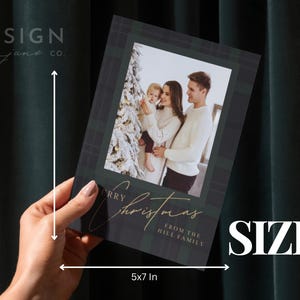 May include: A 5x7 inch rectangular Christmas greeting card featuring a dark green and black plaid border. The center displays a photograph of a family near a Christmas tree. The text reads Merry Christmas from the Hill family in gold script.