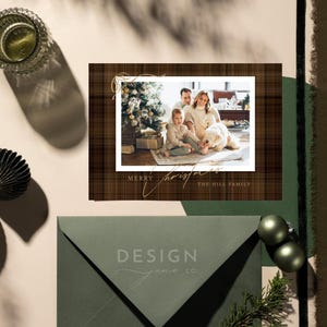 May include: A rectangular holiday greeting card featuring a brown plaid background, a central photograph of a family with a dog near a Christmas tree, and the text Merry Christmas The Hill Family in gold script. An olive green envelope is included.