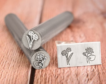 May include: Two metal stamps with floral designs. The stamps are round and have a silver finish. The designs are of two different flowers with stems and leaves. The stamps are shown on a wooden surface.