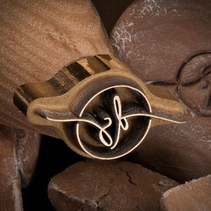 May include: A wooden stamp with a circular design featuring the letters "zf" in a cursive font. The stamp is a light brown color with a dark brown border and is surrounded by other brown objects.