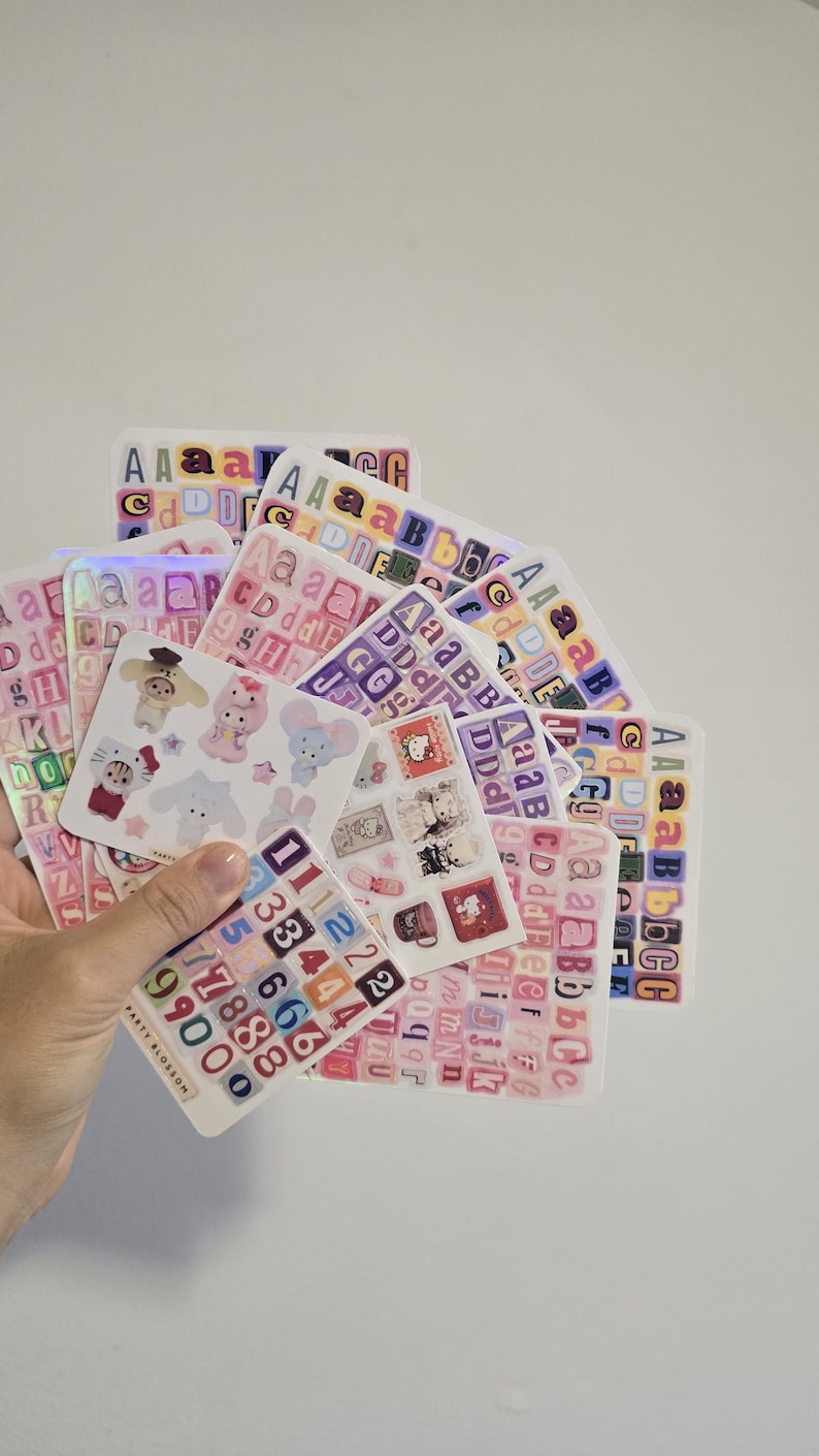 K&ouml;nnte beinhalten: Eine Sammlung von Stickerb&ouml;gen mit bunten Buchstaben, Zahlen und niedlichen Illustrationen. Die Aufkleber zeigen verschiedene Schriftarten und Designs, wobei einige B&ouml;gen holografische Effekte aufweisen. Die Marke "PARTY BLOSSOM" ist auf einem der Stickerb&ouml;gen zu sehen.