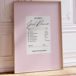 K&ouml;nnte beinhalten: Ein rosa gerahmter Druck mit wei&szlig;em Hintergrund und schwarzem Text, der "Let's Serve Girl Dinner" lautet. Der Text ist wie eine Quittung mit einer Liste von Artikeln und Mengen formatiert, darunter "Olives", "Cherry Tomatoes", "Soft Brie", "Baguette", "Strawberries", "Easy Mac", "Wine & Cheese".
