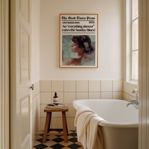 May include: A white bathroom with a framed newspaper print on the wall above a white bathtub. The newspaper headline reads "The Good Times Press" and "An 'everything shower' cures the Sunday blues!"  A wooden stool with a bottle of soap sits next to the bathtub.