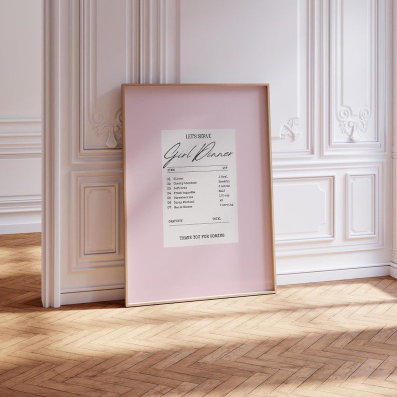K&ouml;nnte beinhalten: Ein rosa gerahmter Druck mit wei&szlig;em Hintergrund und schwarzem Text, der "Let's Serve Girl Dinner" lautet. Der Text ist wie eine Quittung mit einer Liste von Artikeln und Mengen formatiert, darunter "Olives", "Cherry Tomatoes", "Soft Brie", "Baguette", "Strawberries", "Easy Mac", "Wine & Cheese".