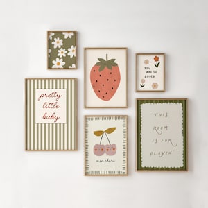 May include: A collection of framed art prints with a whimsical, pastel aesthetic. The prints feature illustrations of a strawberry, cherries, daisies, and text that reads "pretty little baby", "you are so loved", and "this room is for playin'".