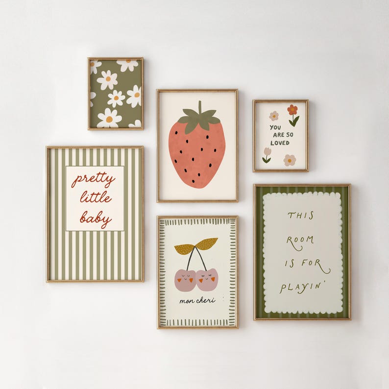 May include: A collection of framed art prints with a whimsical, pastel aesthetic. The prints feature illustrations of a strawberry, cherries, daisies, and text that reads "pretty little baby", "you are so loved", and "this room is for playin'".