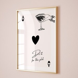 Peut inclure: Une illustration en noir et blanc d'un as de pique avec une main tenant un verre à martini. Le texte "Do it for the plot" est écrit sous la carte.