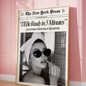 May include: Black and white photo of a woman with a towel on her head, wearing sunglasses and applying lipstick. The photo is framed and has a newspaper headline that reads "I'll Be Ready in 5 Minutes" with the subheading "SAYS WOMAN WHO IS STILL IN THE SHOWER".