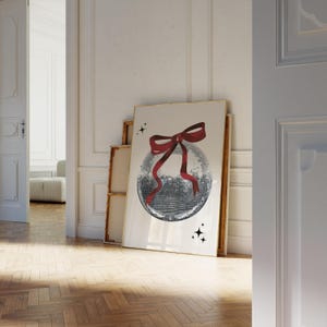 May include: A white framed poster with a silver disco ball with a red bow on top. The disco ball is surrounded by small black stars.
