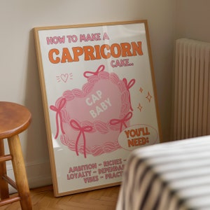 May include: A pink and white illustrated poster with the text "How to make a Capricorn cake." The poster features a heart-shaped cake with the text "Cap Baby" inside. The poster also includes a list of ingredients needed to make the cake, including ambition, riches, loyalty, dependability, vibes, and practice.