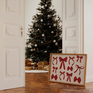 May include: A framed print with a white background and red bow silhouettes. The print is hanging on a white wall next to a decorated Christmas tree.