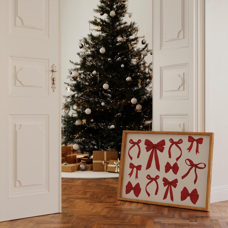 May include: A framed print with a white background and red bow silhouettes. The print is hanging on a white wall next to a decorated Christmas tree.