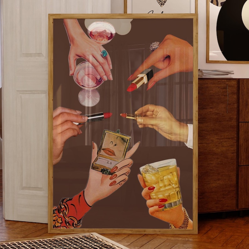 May include: A framed artwork featuring hands holding lipstick, a compact mirror, a cocktail, and a glass of wine. The hands are adorned with rings and red nail polish. The background is a solid brown color.