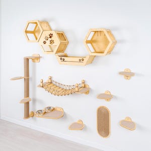 Pode incluir: Um conjunto de móveis para gatos em madeira clara montado numa parede branca. O conjunto inclui prateleiras hexagonais, uma ponte, um poste de arranhar e várias plataformas. Recortes de pegadas decoram algumas peças. O conjunto foi concebido para que os gatos subam e brinquem.