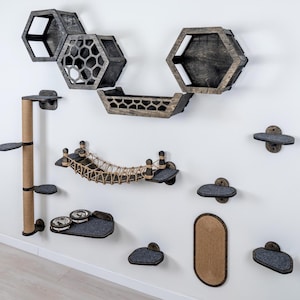 May include: A collection of cat furniture mounted on a white wall. The set includes hexagon-shaped shelves, a bridge, a scratching post, and various platforms. The pieces are made of wood and gray felt, with a natural rope bridge.