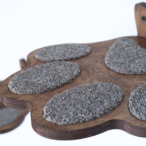May include: Wooden cat furniture with a paw-shaped design. The dark brown wood has six oval-shaped, gray carpeted pads for the cat to rest on. The cat furniture is mounted on a white background.