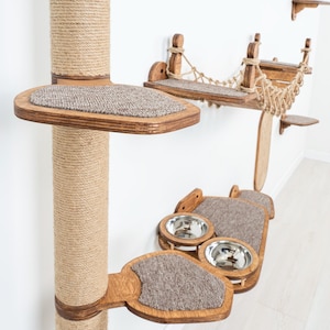 May include: A multi-level cat tree with a sisal-wrapped post, wooden platforms, a hammock, and food bowls. The platforms have a carpeted surface. The cat tree is made of wood and rope, and is designed to be mounted on a wall.