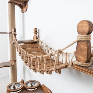 May include: A wooden cat tree with a bridge, scratching post, and platforms. The bridge is made of wooden slats and rope. The scratching post is wrapped in sisal rope. The platforms have a carpeted surface. The cat tree is stained a medium brown color.
