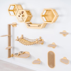 May include: A wooden cat furniture set mounted on a white wall. The set includes hexagon-shaped shelves, a bridge, a scratching post, and various platforms. Some pieces feature paw print cutouts. The set is made of light-colored wood.