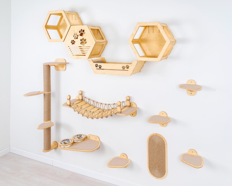 May include: A wooden cat furniture set mounted on a white wall. The set includes hexagon-shaped shelves, a bridge, a scratching post, and various platforms. Some pieces feature paw print cutouts. The set is made of light-colored wood.