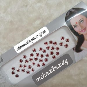 Può includere: Un foglio di adesivi bindi rossi e argentati con il testo "stimulate your ajna" e "mehndibeauty".